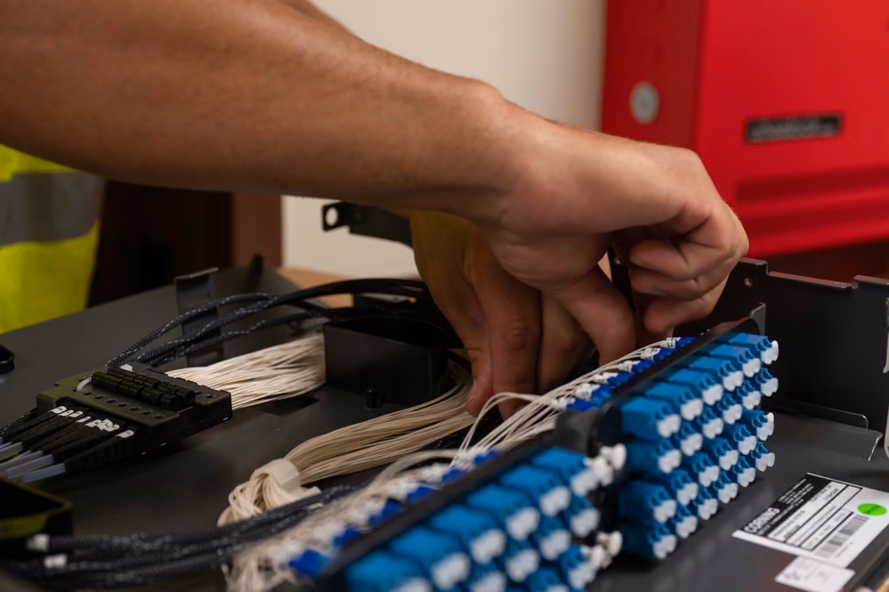 A network technician connecting fiber-optic cables to a rack-mounted termination panel.