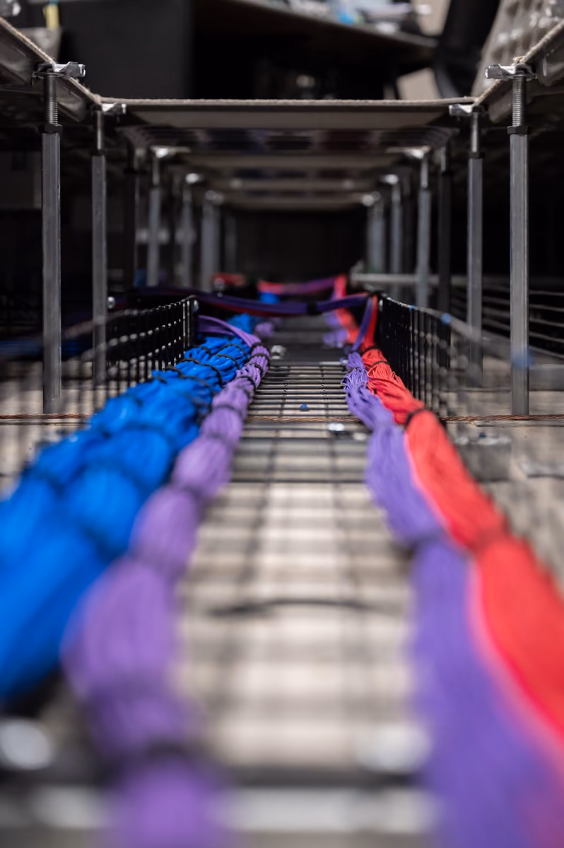 Bundles of color-coded fiber-optic cable routed beneath a raised operations-room floor.