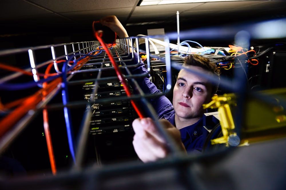 A technician adjusting dense network cabling between equipment racks in a server room.