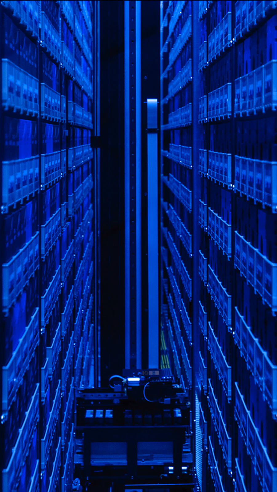 A blue-lit robotic tape archive aisle with cartridge racks rising on both sides.