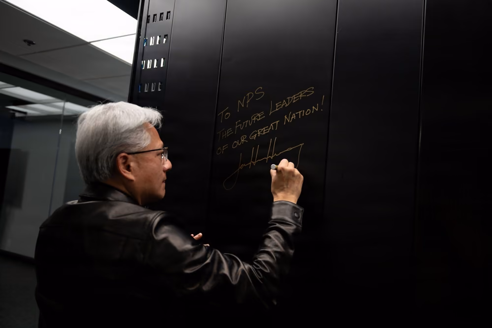 NVIDIA CEO Jensen Huang writes a dedication on the closed door of a black DGX GB300 system cabinet at the Naval Postgraduate School.