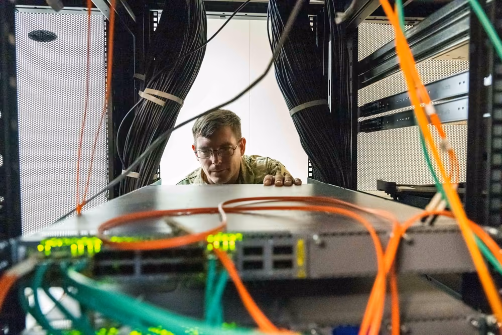 A technician inspecting cabling and components at the rear of a populated server rack.