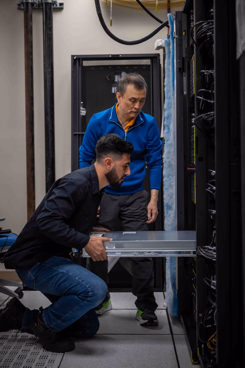 Technicians installing high-performance computing equipment into a tall server rack.