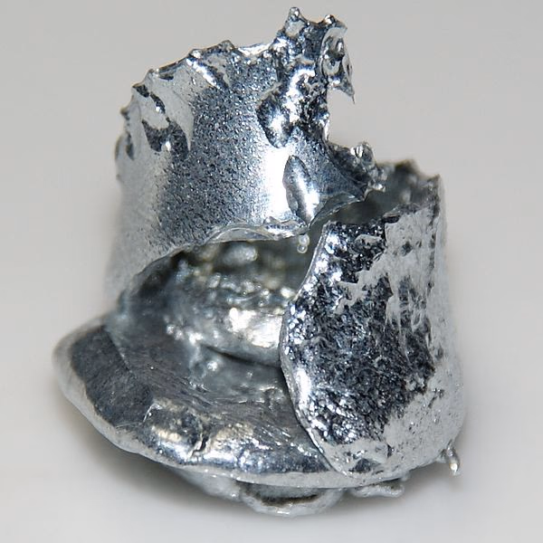 A silvery piece of solid elemental gallium with an irregular folded surface.