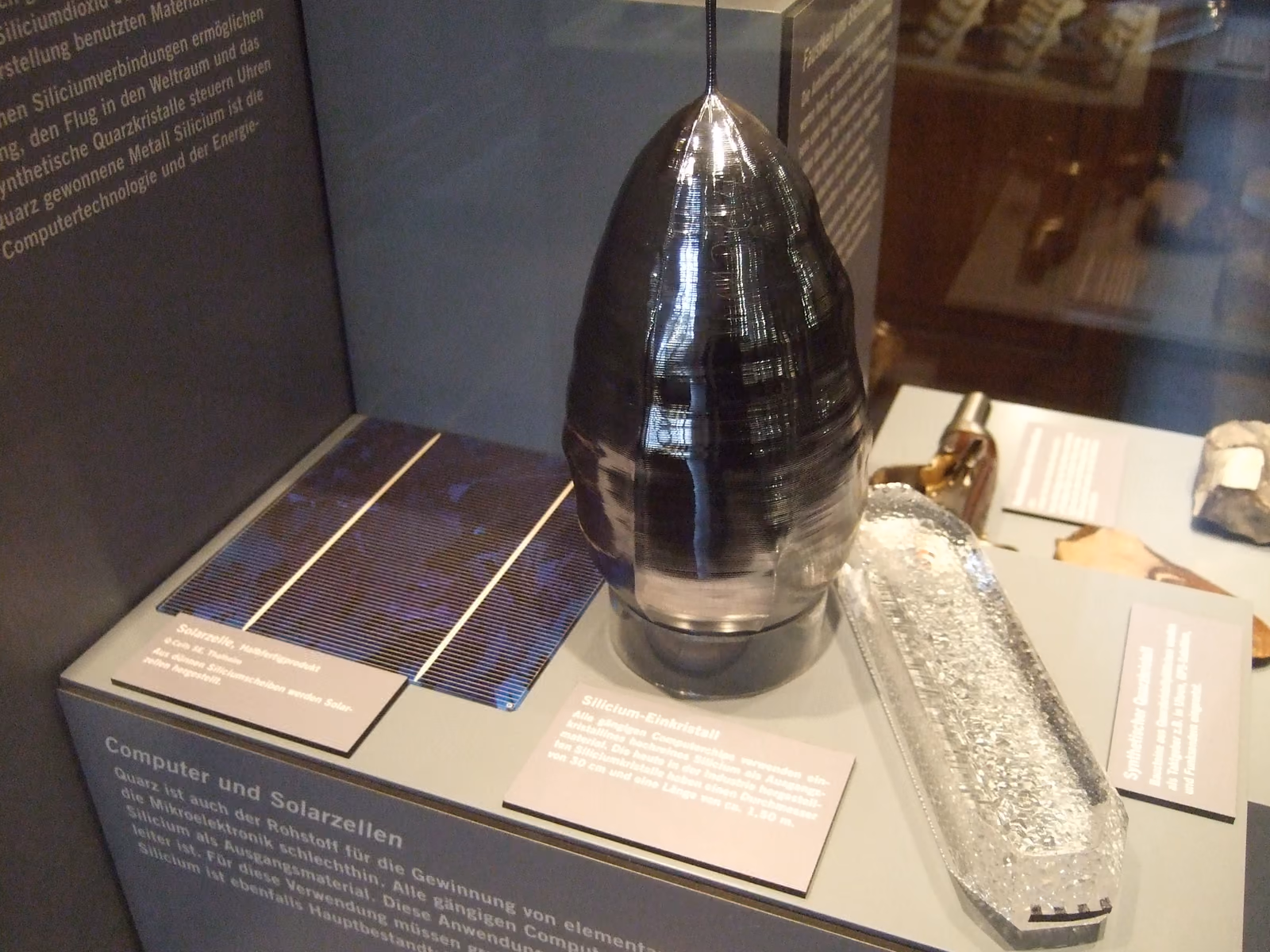 A cylindrical single-crystal silicon boule displayed upright in a museum case.