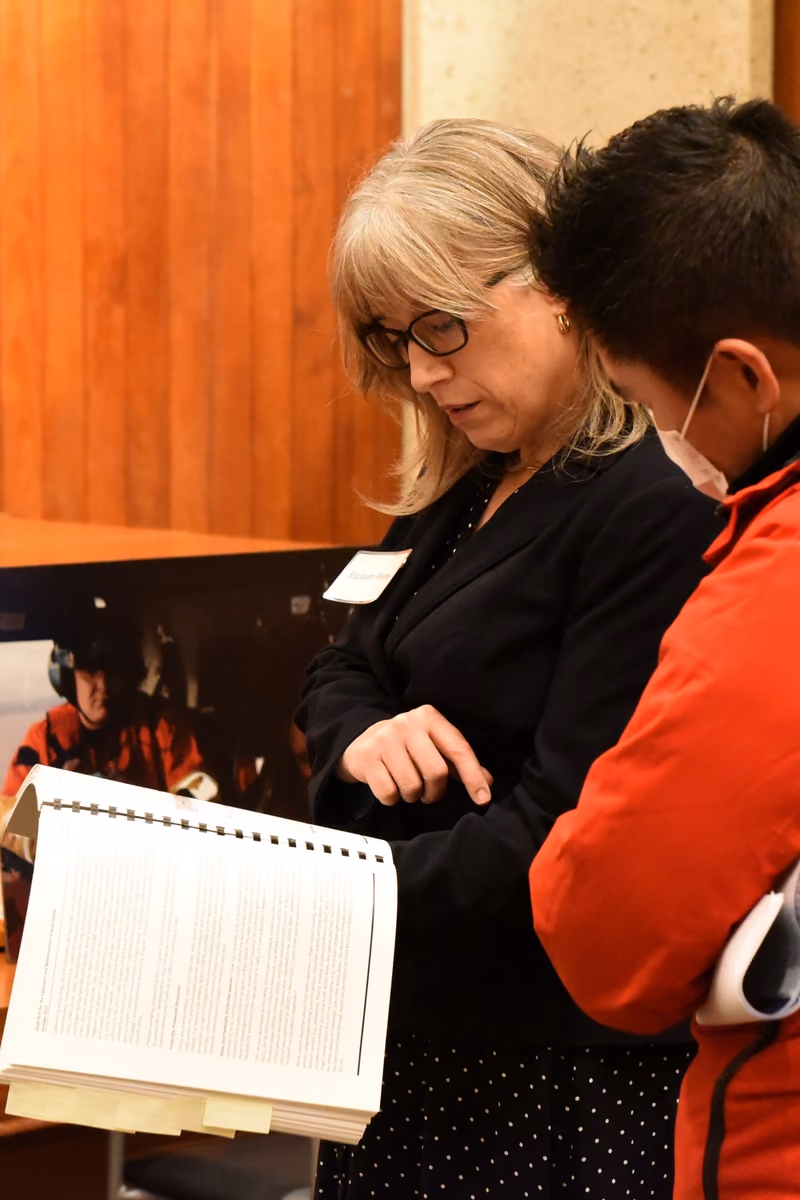 An environmental specialist discussing project-impact display boards with a member of the public at a meeting.