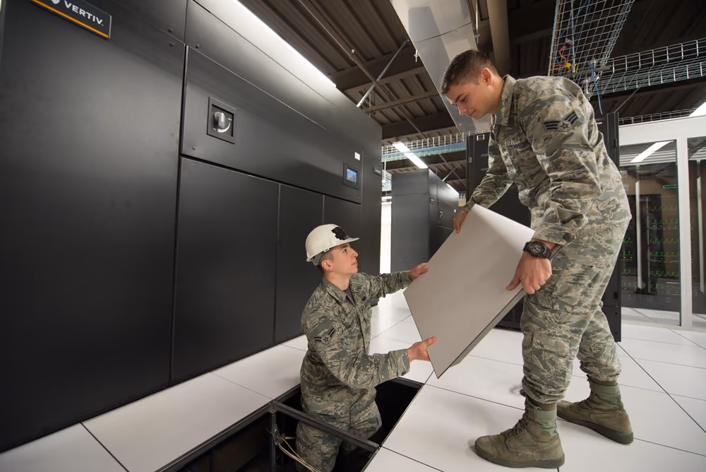 Technicians working beside raised-floor panels and computer-room cooling equipment in an HPC data center.