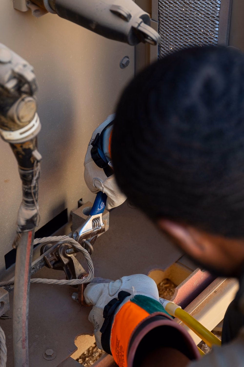 An electrician wearing protective equipment tightens a connection inside electrical distribution equipment.
