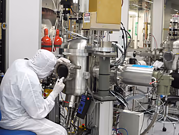 A cleanroom worker inspecting a semiconductor wafer inside process equipment.
